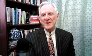 Photo of Dennis McCuistion speaking into a microphone with books behind him.